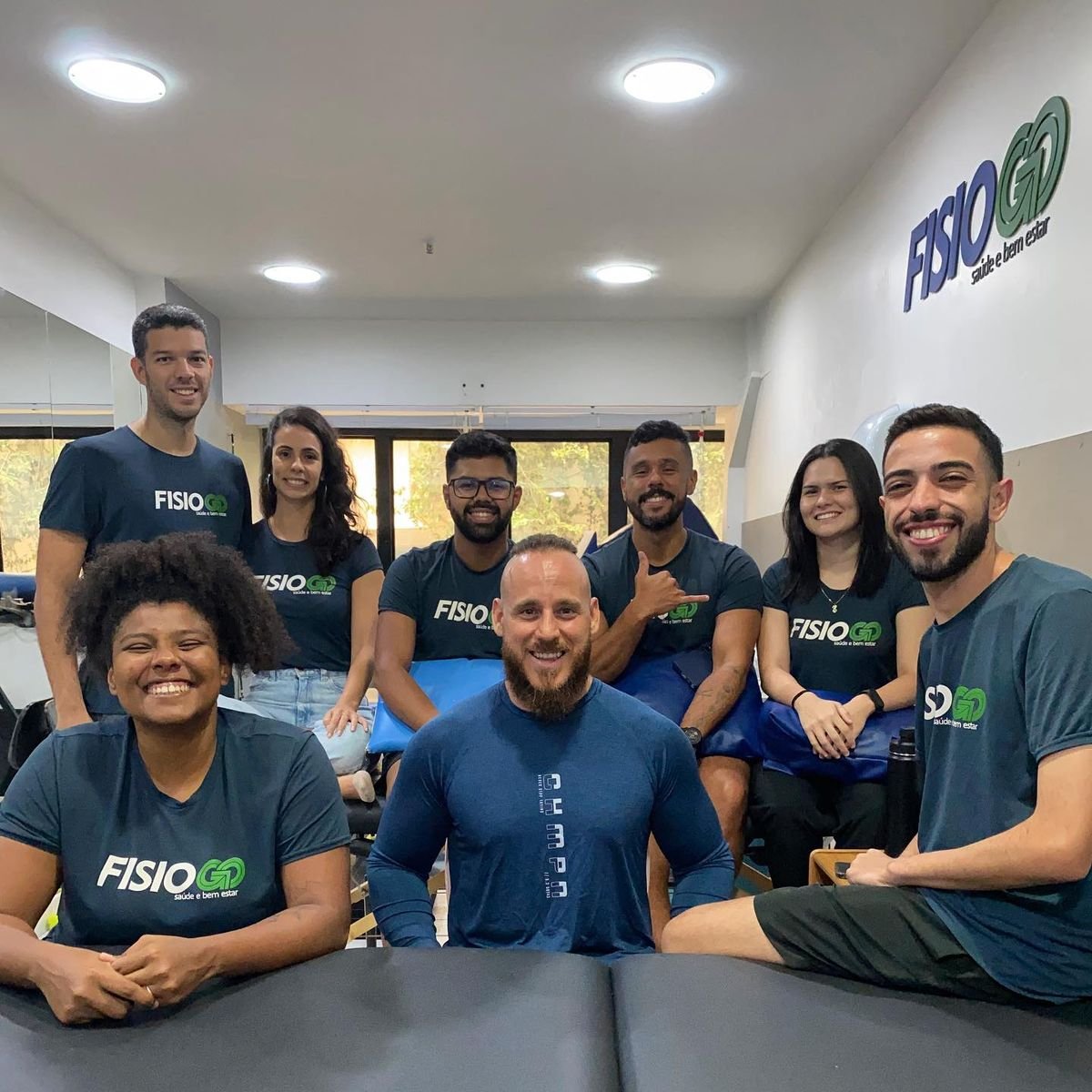 Equipe da FisioGo reunida na clínica, com a parede do logo ao fundo